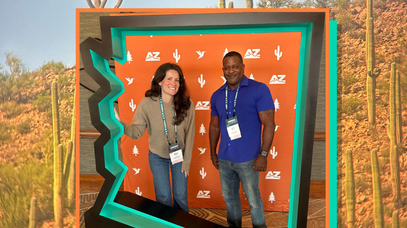 Mady and Larry inside an Arizona state shaped photo booth, with a cactus scene behind.
